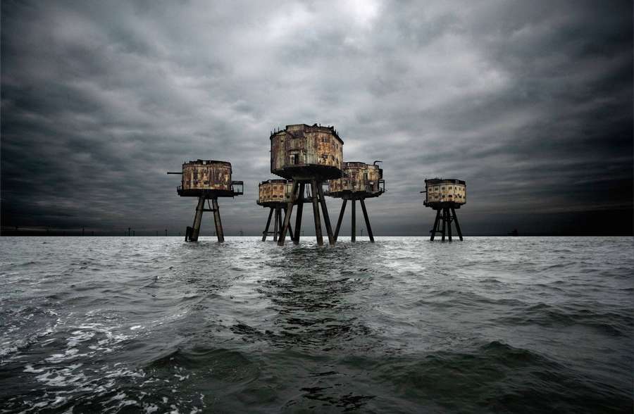 Abandoned wooden structures in stormy ocean under dark sky — UK Wallpaper