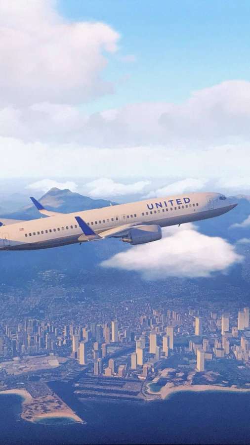 United Airlines plane flying over a coastal city with mountains in the distance. — United Background