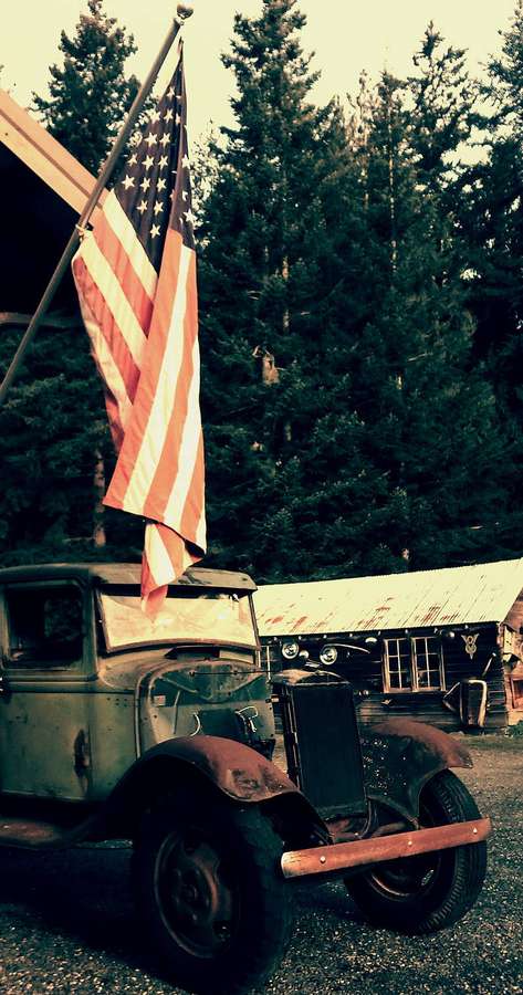 Old rusty truck with American flag in front of cabin in pine forest — USA Flag Background
