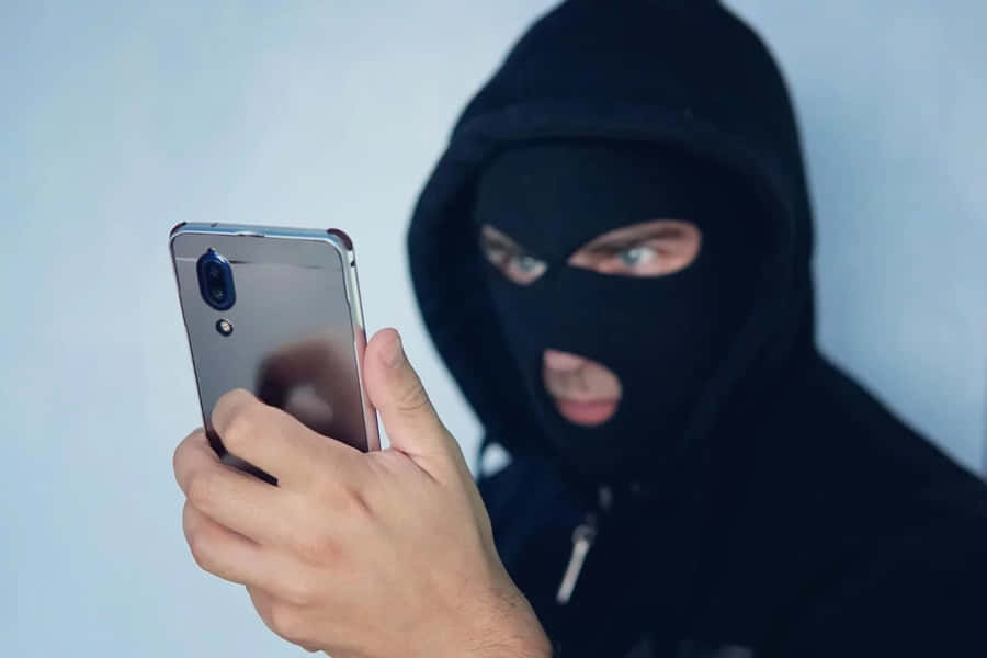 Person i svart hettegenser og maske holder smarttelefon med intenst blikk. — Utpressing Bakgrunner