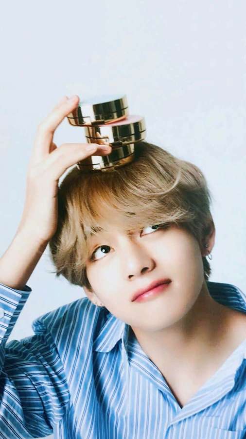 Young man balancing golden cosmetic jars on his head in a blue striped shirt. — V Bts Phone Wallpaper