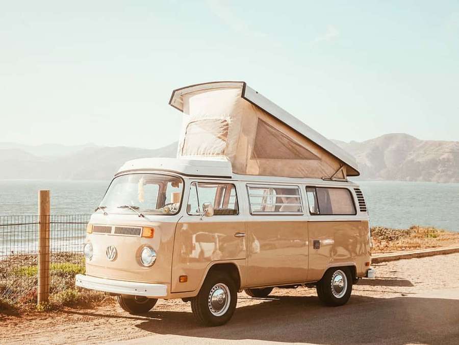 Vintage beige camper van parked by the ocean with mountains in the background. — Van Picture