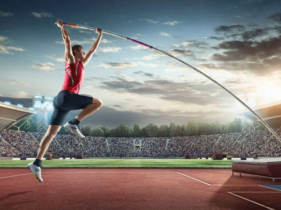 Athlete pole vaulting at sunset in stadium with cheering crowd. — Vault Picture
