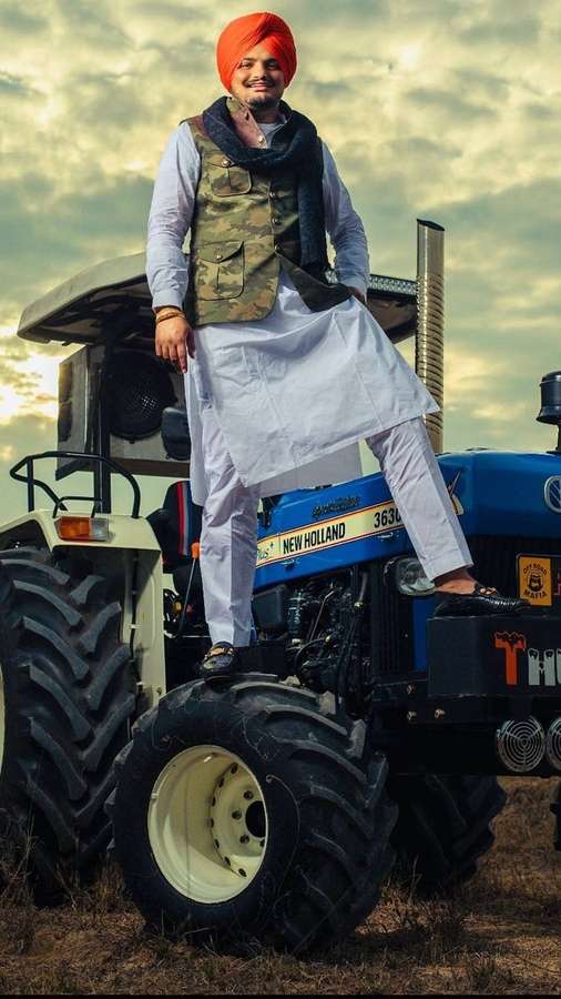 Un hombre con turbante naranja posa sobre un tractor azul al atardecer. — Video musical Fondos de pantalla