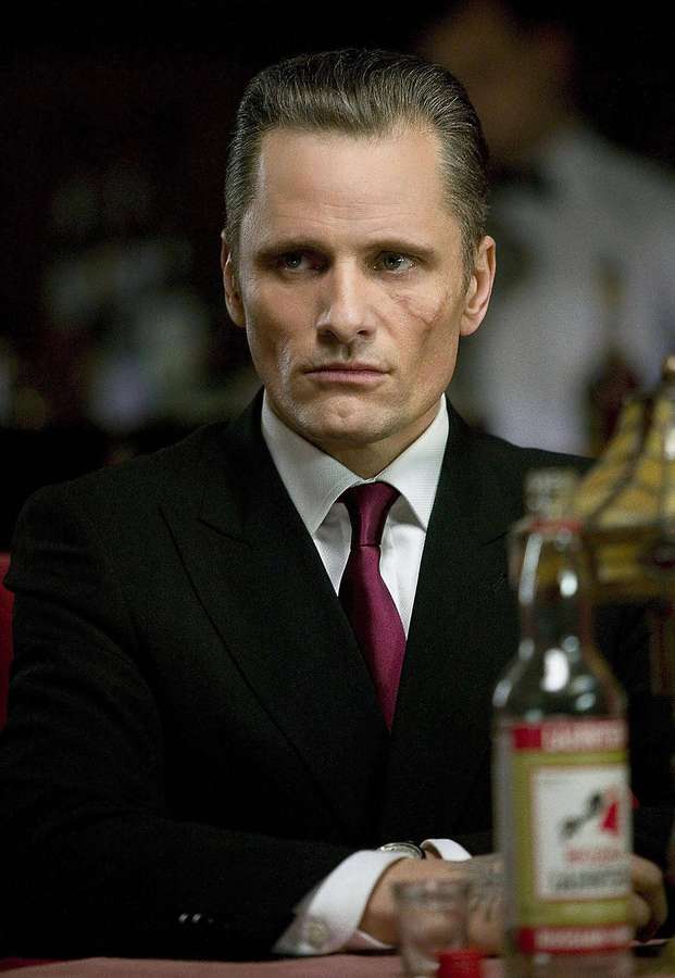 Mann im Anzug mit Narbe sitzt an der Bar und hält Flasche — Viggo mortensen Bilder