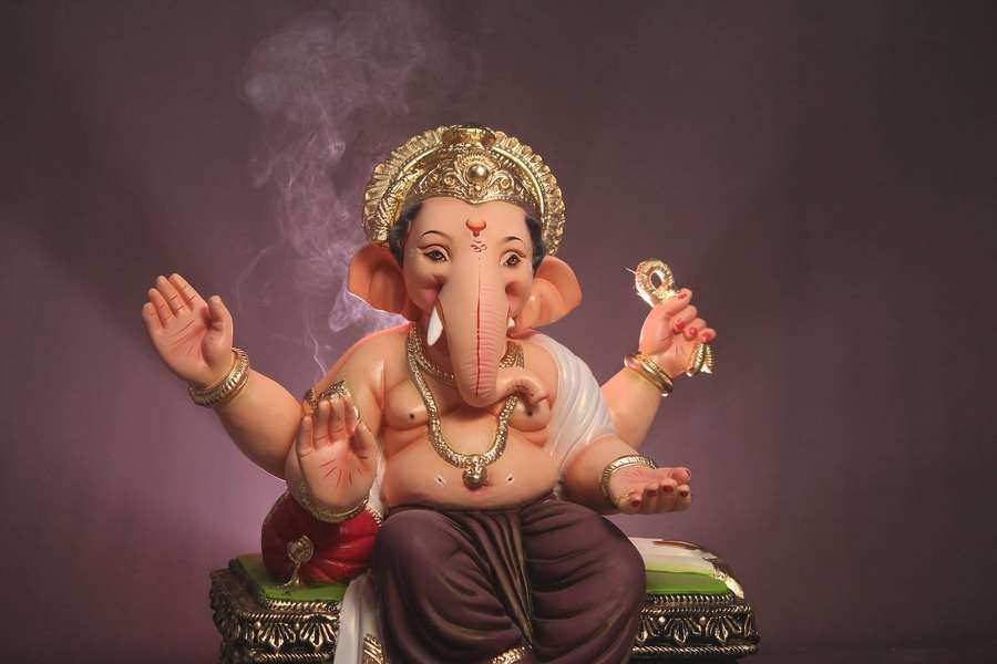 Colorful Ganesha statue seated on ornate throne with smoke rising behind. — Vinayaka Wallpaper
