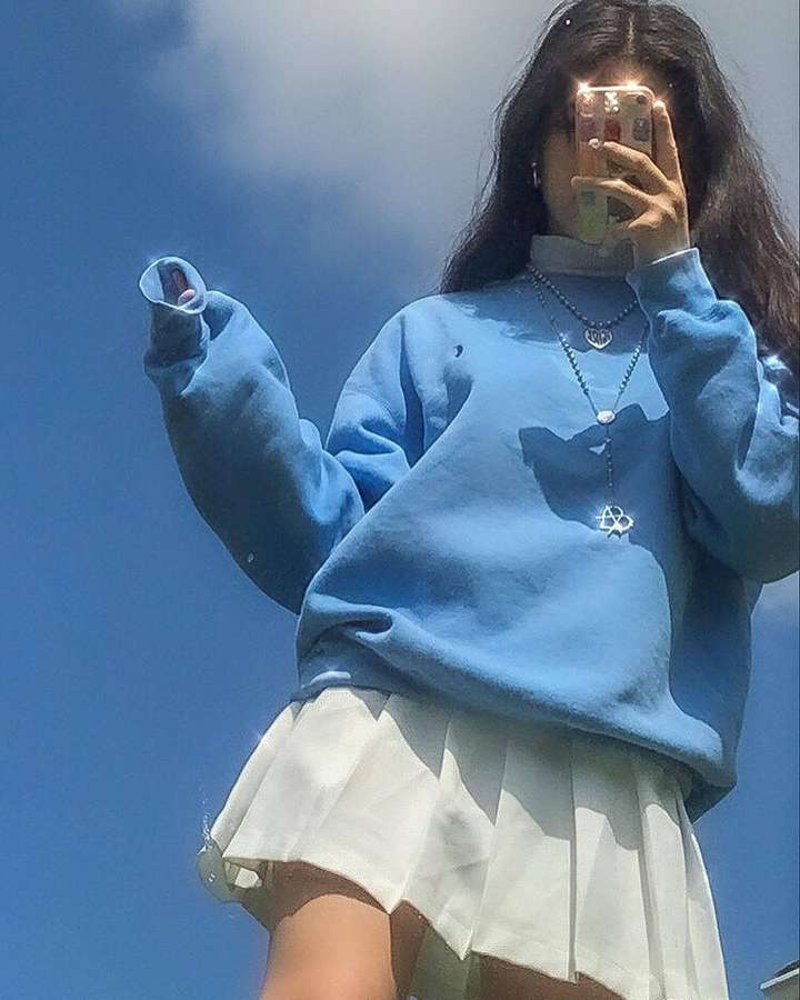 Pessoa de moletom azul e saia branca tirando selfie no espelho ao ar livre sob céu azul. — Vista do céu Papéis de Parede