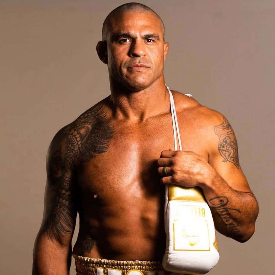 A tattooed male boxer holding a white and gold glove in a studio setting. — Vitor Belfort Wallpaper