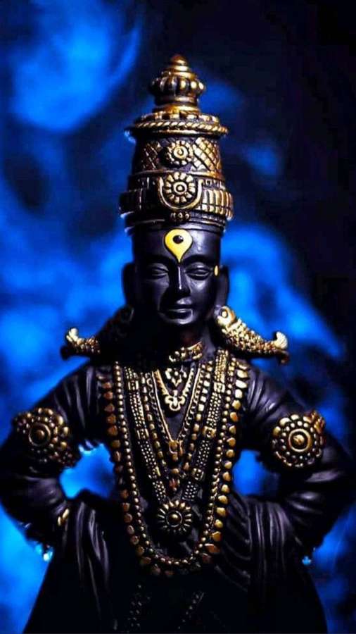 Eine dunkelhäutige Götterstatue mit Goldschmuck vor einem blau leuchtenden Hintergrund. — Vitthal Bilder