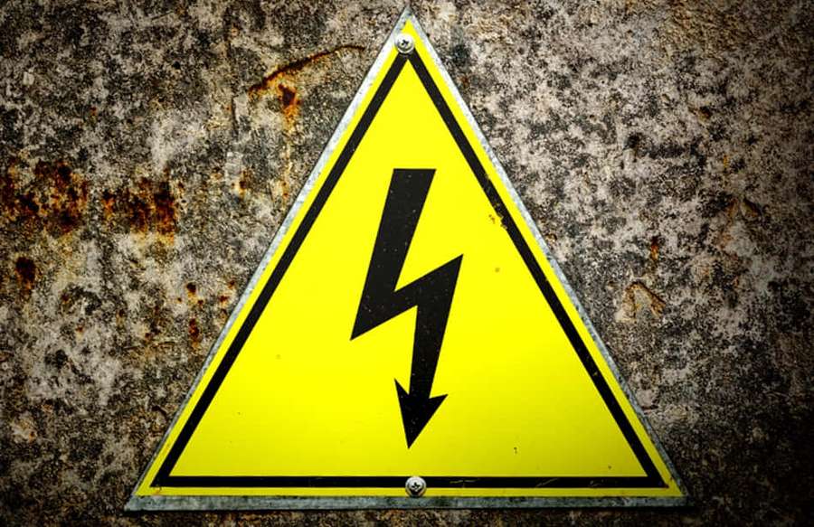 Warning sign indicating electrical hazard on weathered metal. — Voltage Picture