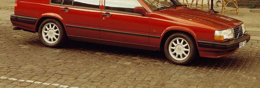 Red station wagon parked on cobblestone street near wooden chairs. — Volvo 740 Wallpaper