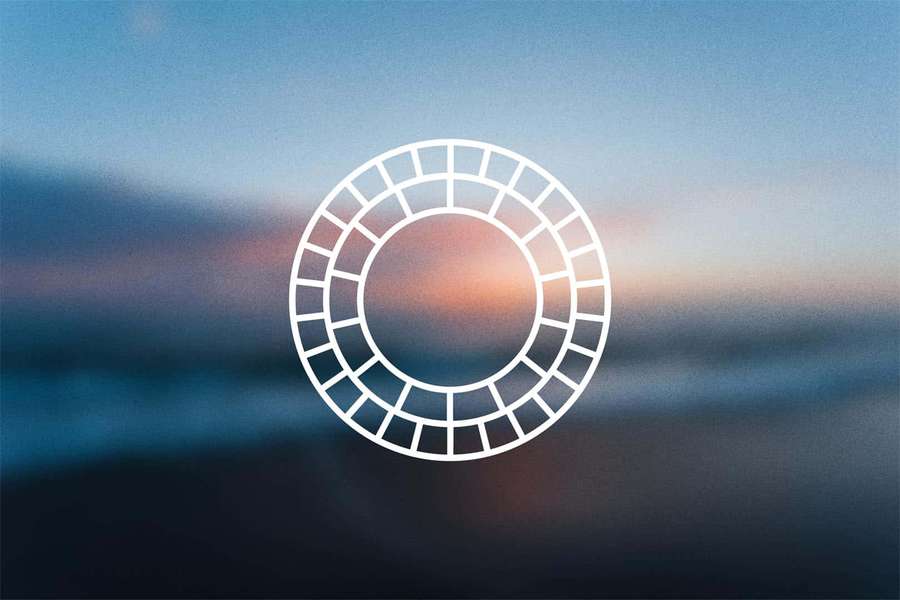 A white circular grid logo against a blurred sunset sky gradient. — Vsco Background