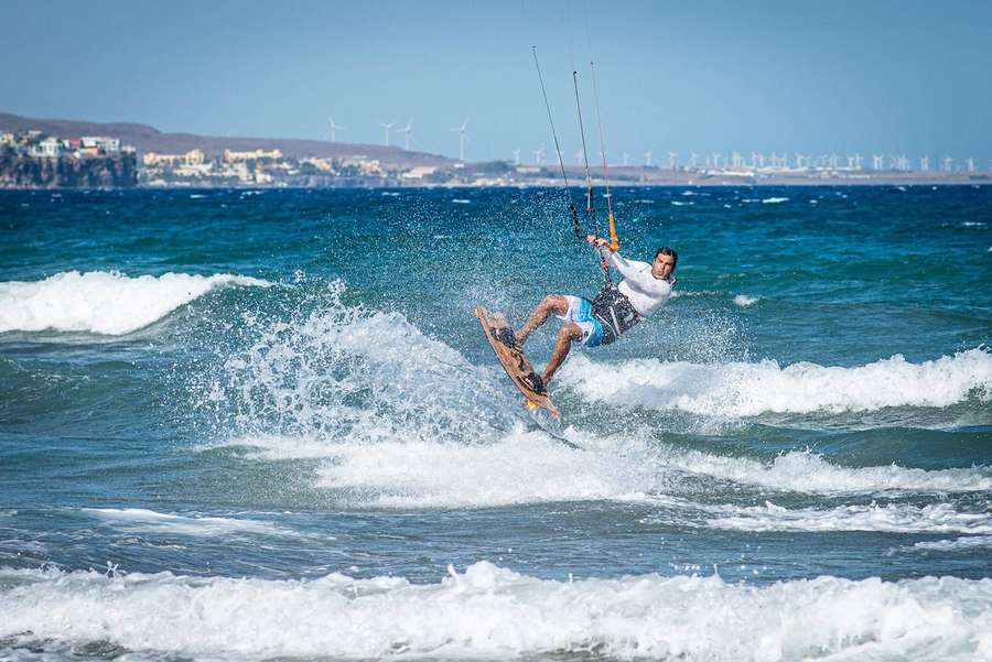Kitesurfer surfando uma onda com turbinas eólicas num penhasco ao fundo. — Wakeboard Papéis de Parede
