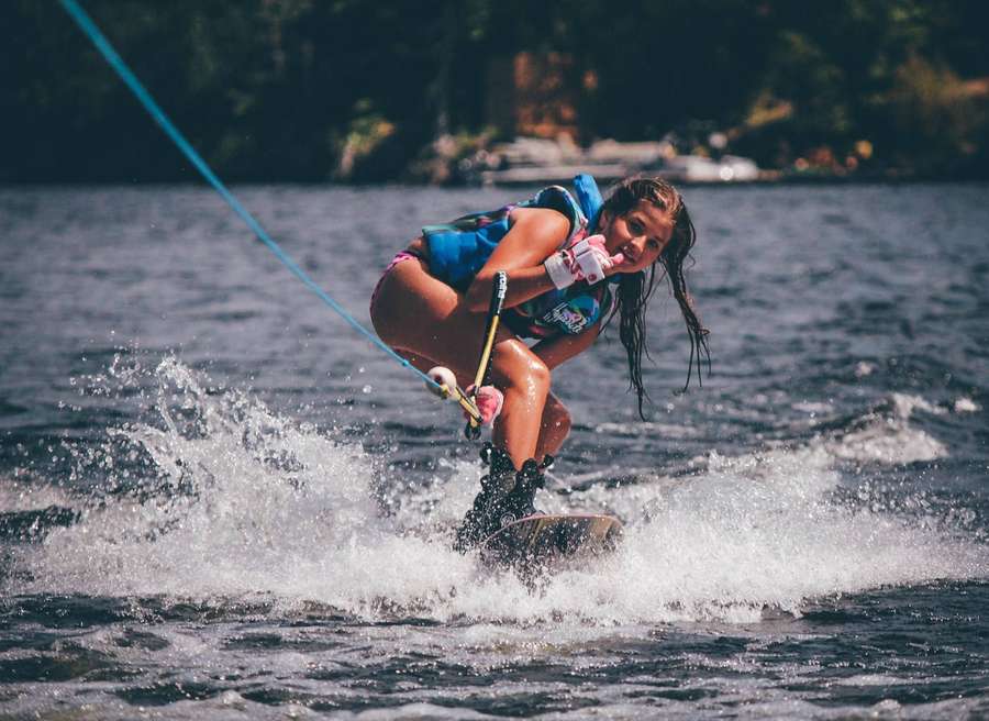 Junge Frau beim Wasserski auf einem sonnigen See mit Bäumen im Hintergrund. — Wakeboarden Wallpaper