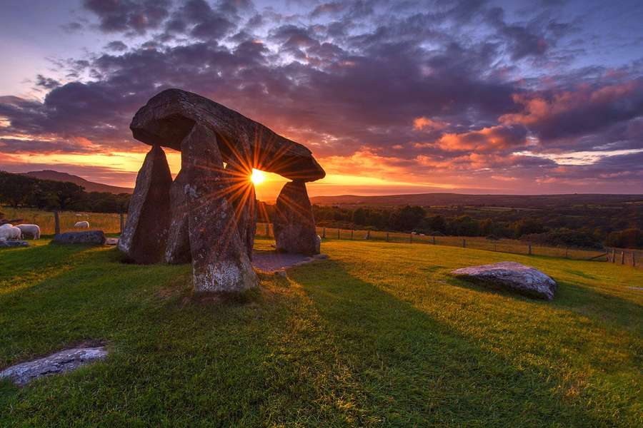 Ancient stone circle with sunburst at sunset over grassy field with sheep — Wales Wallpaper