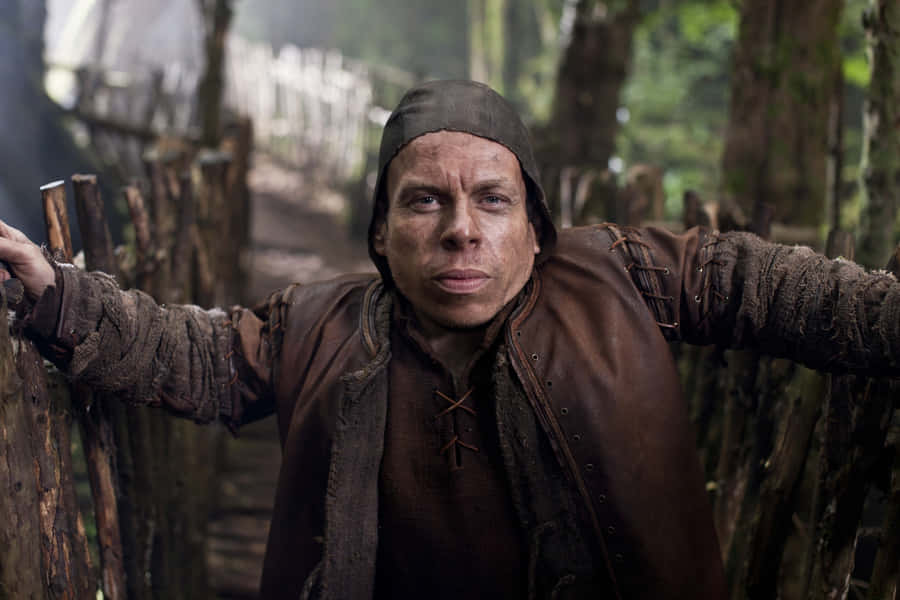 Mies mutaisissa keskiaikaisissa vaatteissa nojaa puuaitaan metsässä. — Warwick Davis Taustakuvat