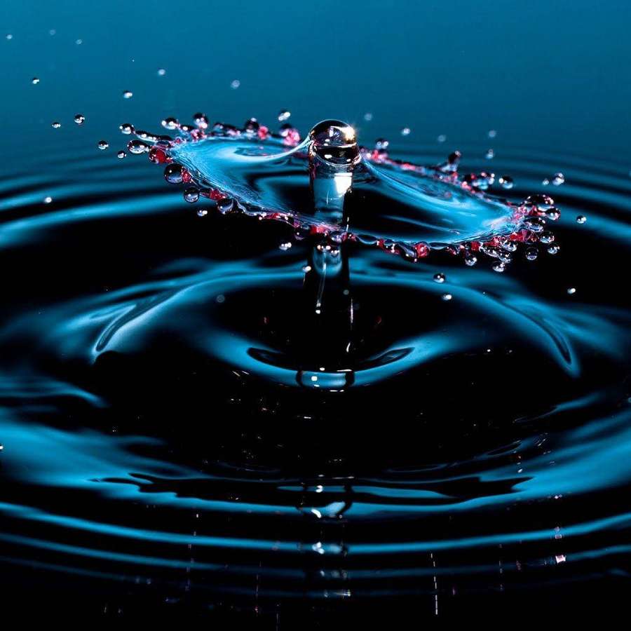 Ein Wassertropfen erzeugt Wellen in dunkelblauer Flüssigkeit mit funkelnden Tropfen. — Wasser Desktop Wallpaper