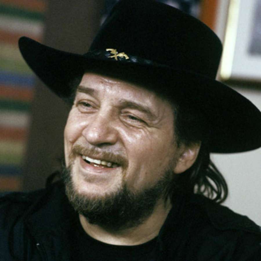 A bearded man in a black hat smiles warmly indoors. — Waylon Jennings Wallpaper