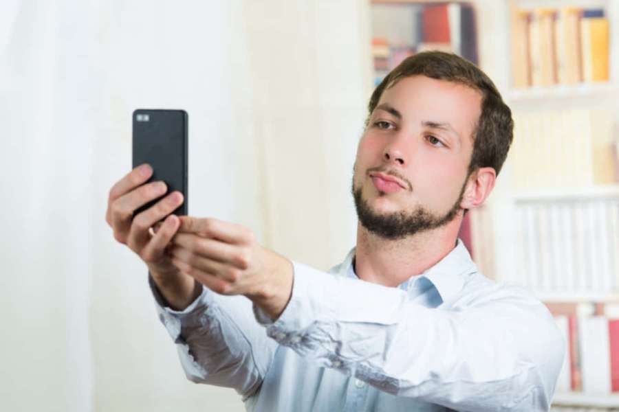 Man taking selfie with phone in room with bookshelves — Weird Profile Picture