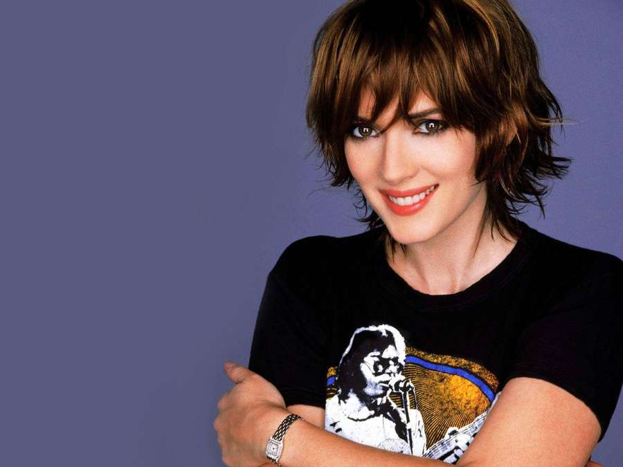 Uma mulher com cabelo curto castanho sorri enquanto usa uma camiseta gráfica preta e um relógio. — Winona ryder Papéis de Parede