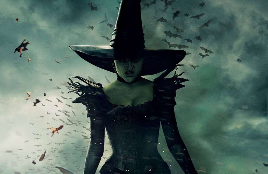 Eine Hexe mit einem breitkrempigen Hut, umgeben von fliegenden Fledermäusen an einem stürmischen Himmel. — Witch Wallpaper