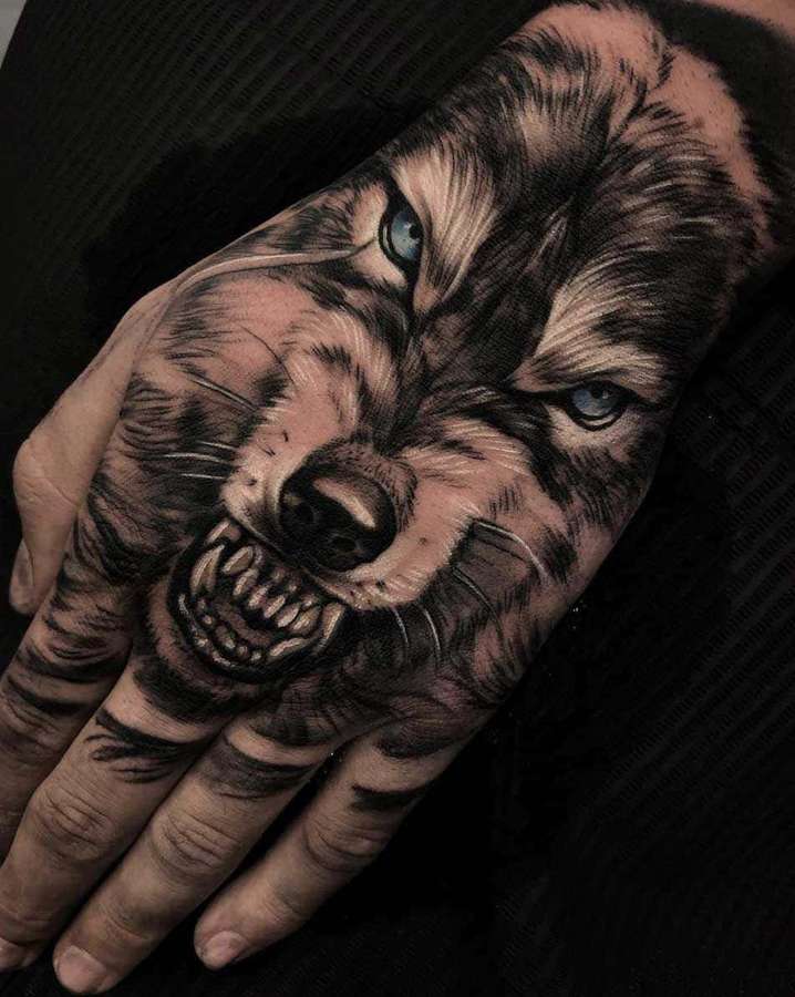 A hand tattooed with a fierce wolf face showing sharp teeth and blue eyes. — Wolf Tattoo Wallpaper