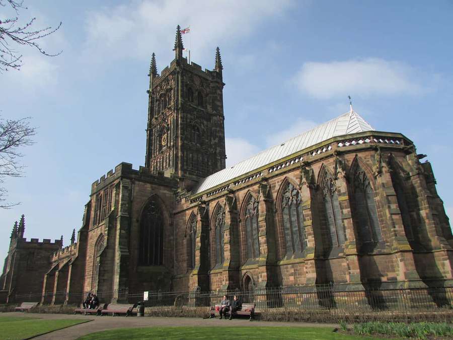 Menschen sitzen auf Bänken vor einer großen historischen Steinkathedrale unter blauem Himmel. — Wolverhampton England Wallpaper