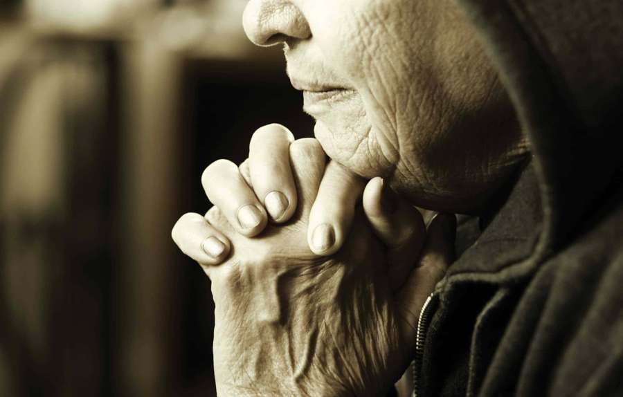 An elderly person clasps hands near their face in a moment of quiet contemplation. — Woman Praying Background