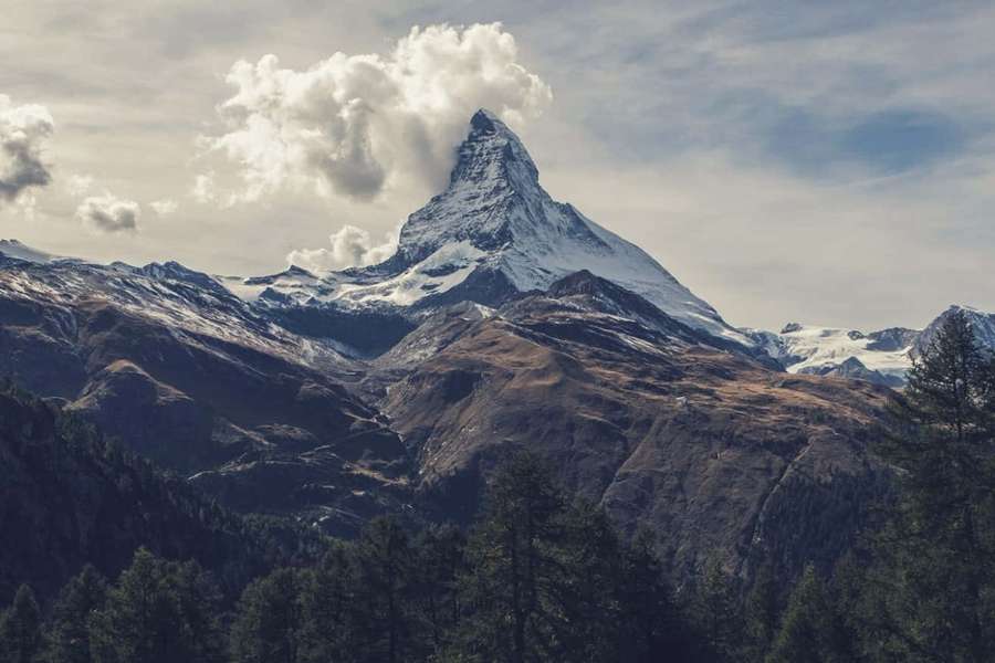 Verschneiter Berggipfel mit Wolken und Wald darunter — Wunderschöne Bergbilder