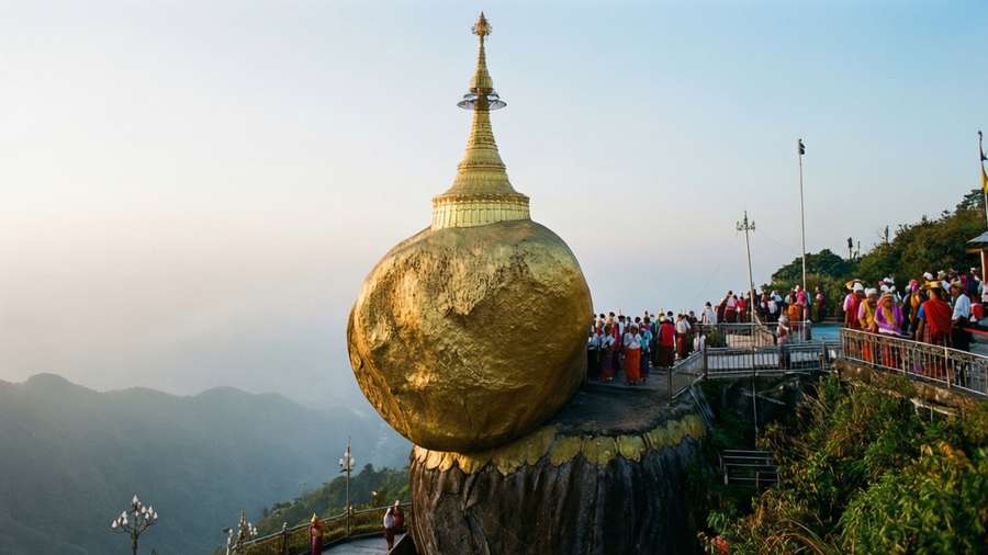 Golden pagoda perched on a cliff with visitors below at sunset. — Yangon Background