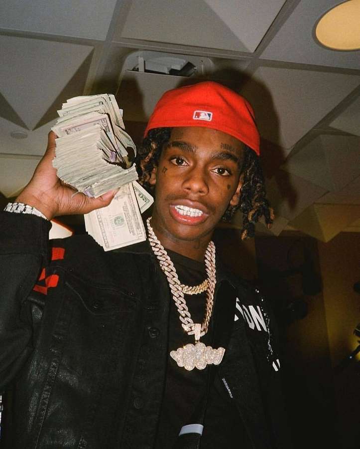Young man holding a stack of cash and wearing a diamond chain and red cap. — Ynw Background