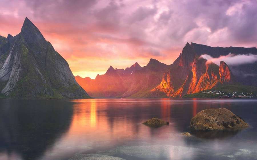 Jagged mountains reflect fiery sunset colors in calm water with misty peaks and small village. — Yosemite Wallpaper