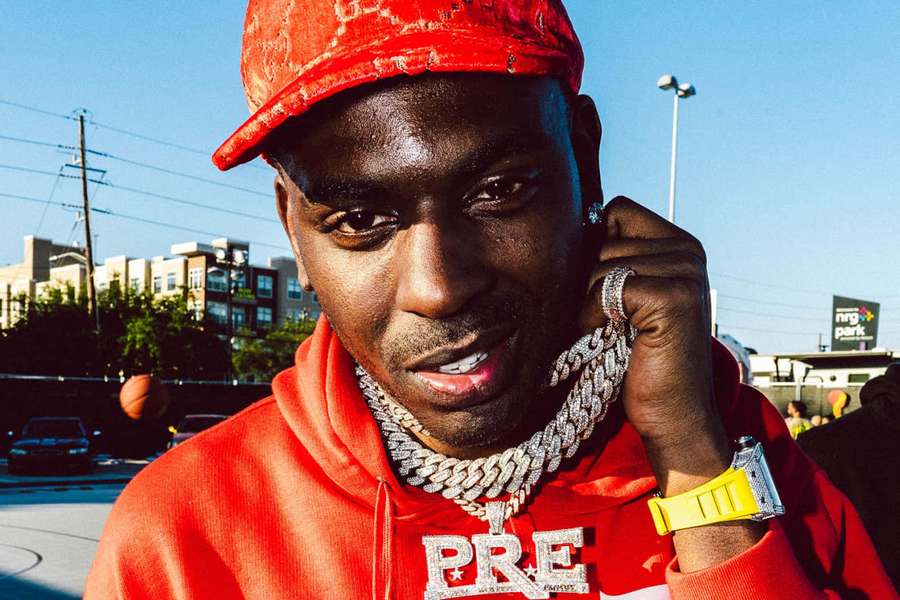 Man in red hoodie and cap wearing gold chain and yellow watch outdoors. — Young Dolph Background