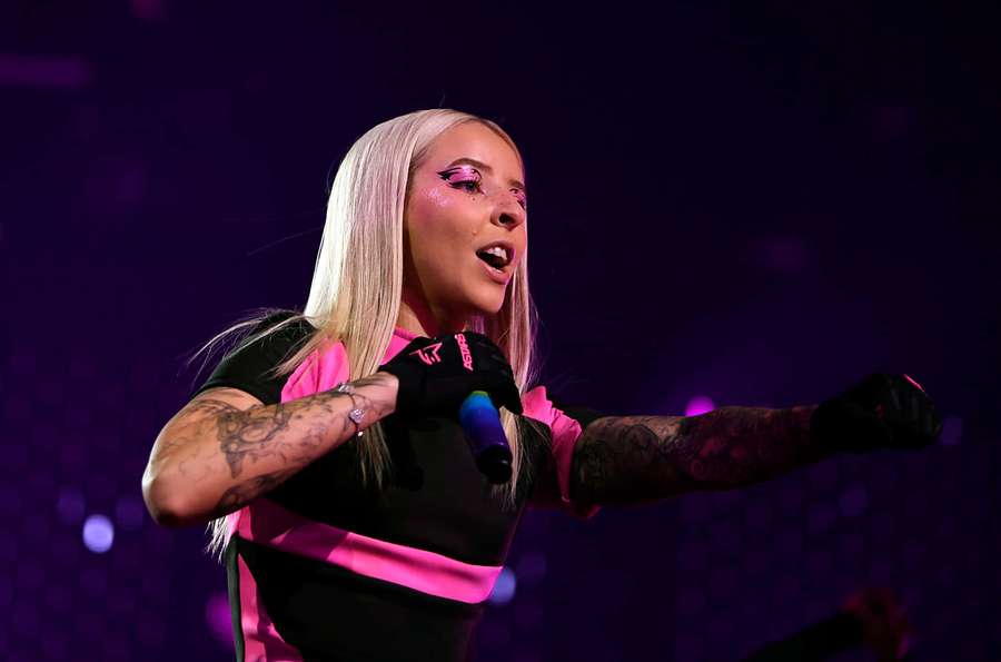 Blonde singer with tattoos performing on a purple lit stage. — Young Miko Wallpaper