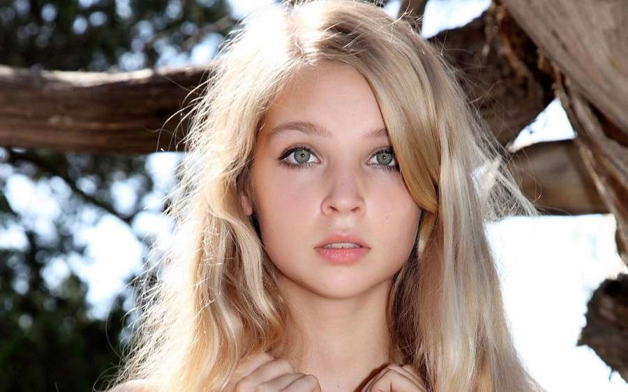 Junge blonde Frau mit grünen Augen steht unter Bäumen im hellen Sonnenlicht. — Young Models Bilder