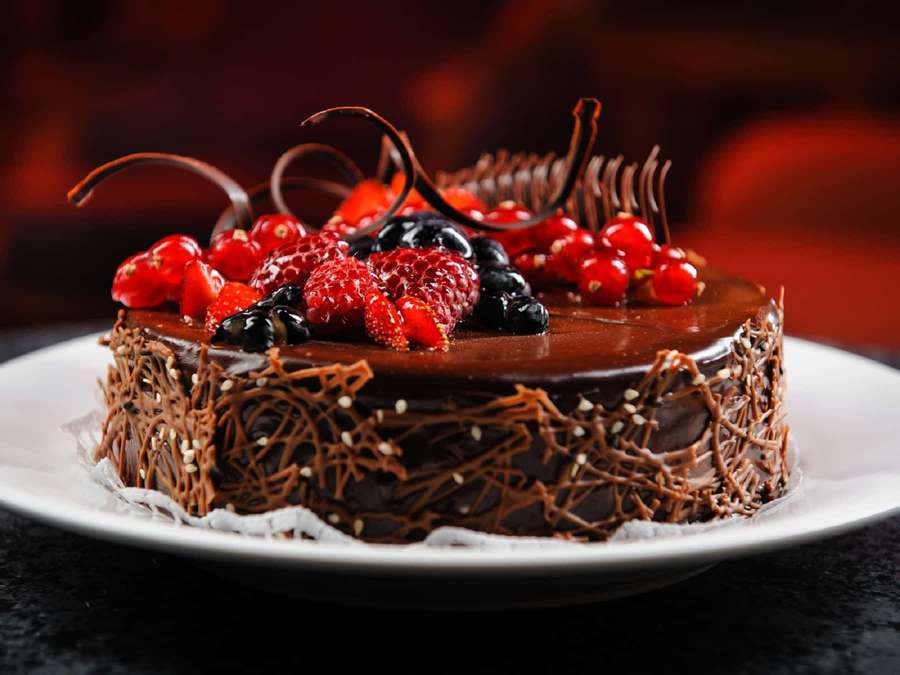 Rich chocolate cake topped with strawberries blueberries and red currants on a white plate. — Yummy Wallpaper