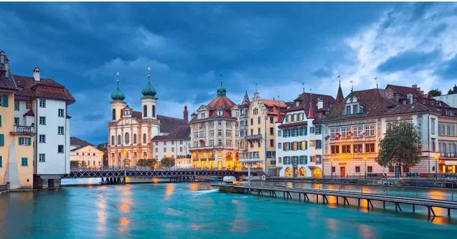 Historic European buildings lit up at twilight reflected in a calm river. — Zurich Wallpaper