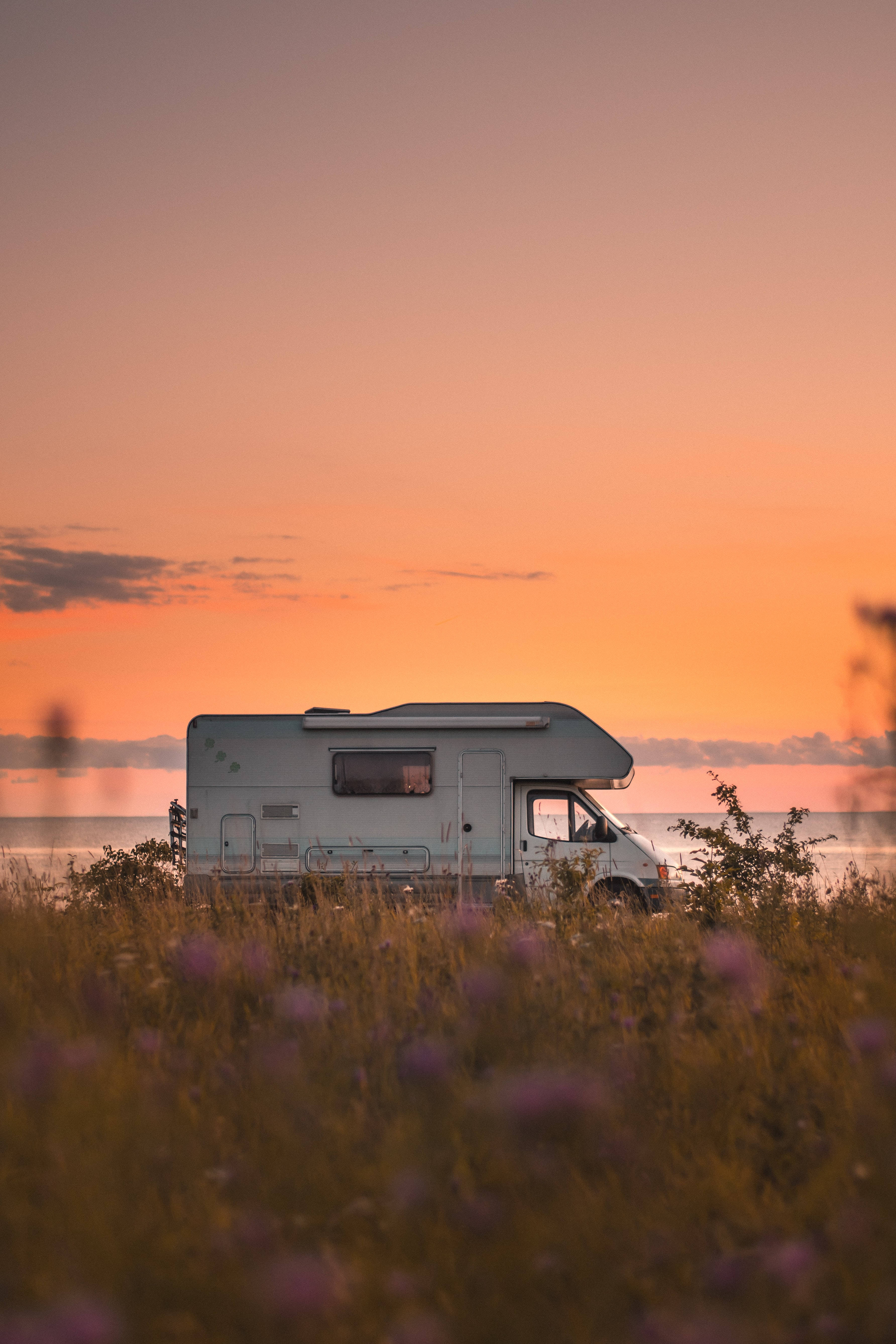 A Camper Parked In A Field At Sunset Background