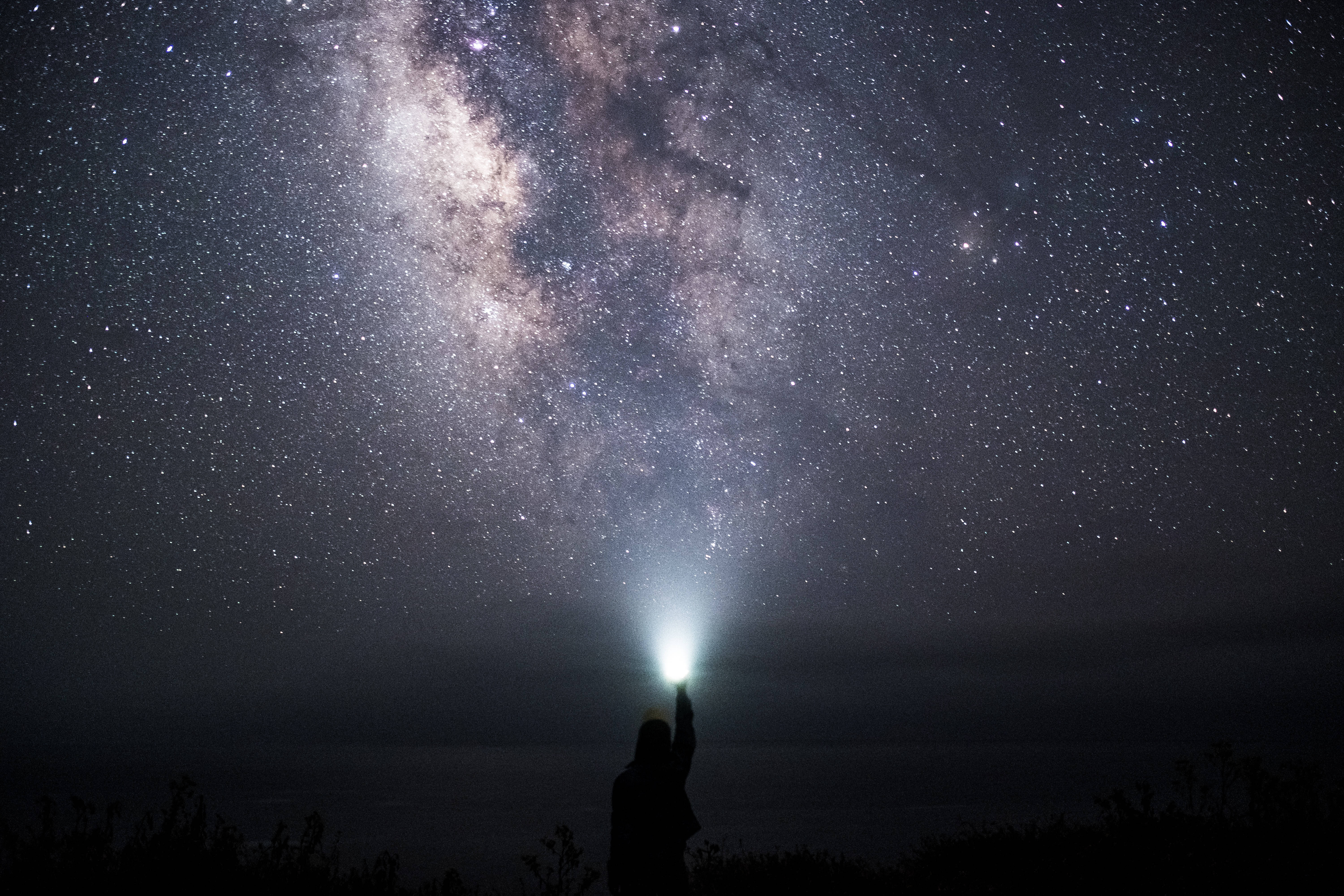 A Person Holding A Flashlight Up To The Milky Background