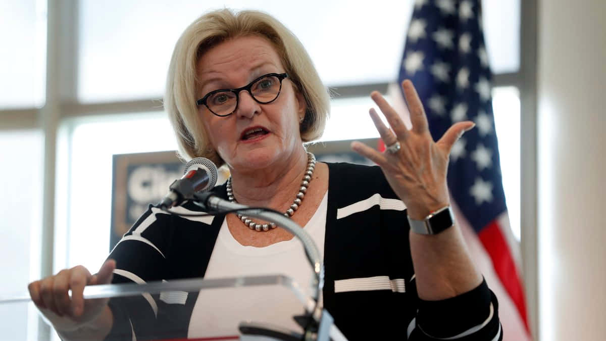 Download Claire Mccaskill Gesturing With Us Flag Wallpaper | Wallpapers.com