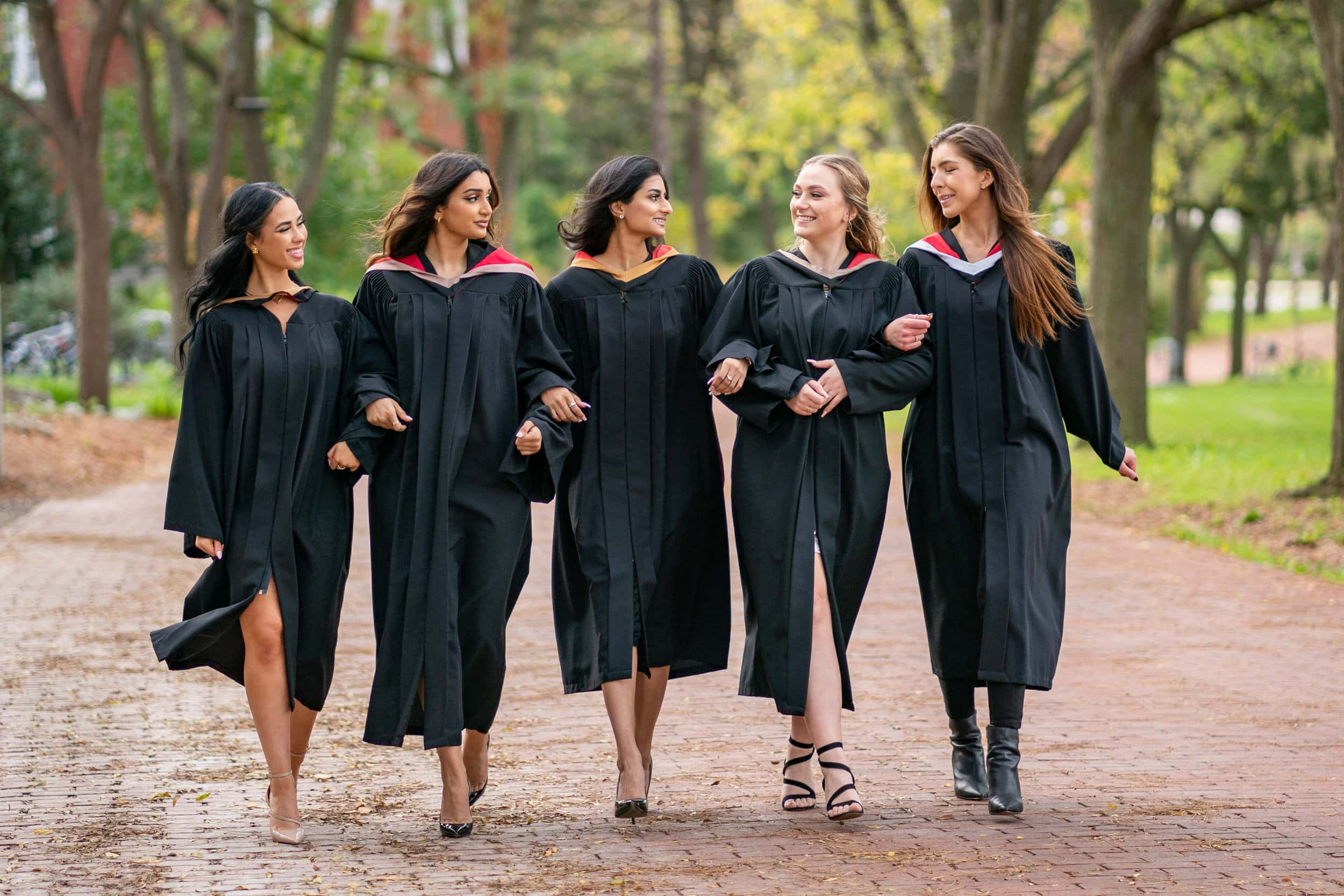 Descargar Cuatromujeres Con Togas De Graduación Negras Caminando Juntas