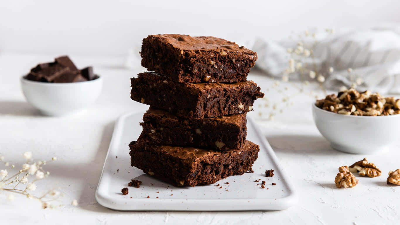 A Stack Of Brownies With Walnuts On A White Plate