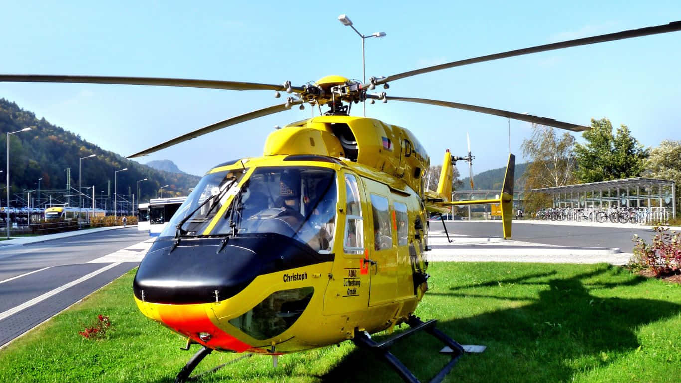 En gul helicopter parkeret på græsset nær et bygning