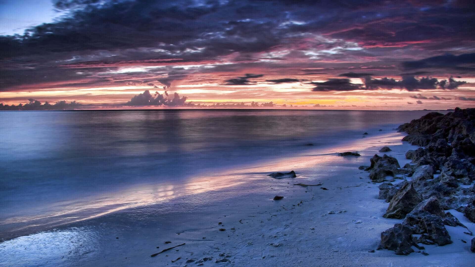 En solnedgang over en strand med klipper og vand Wallpaper