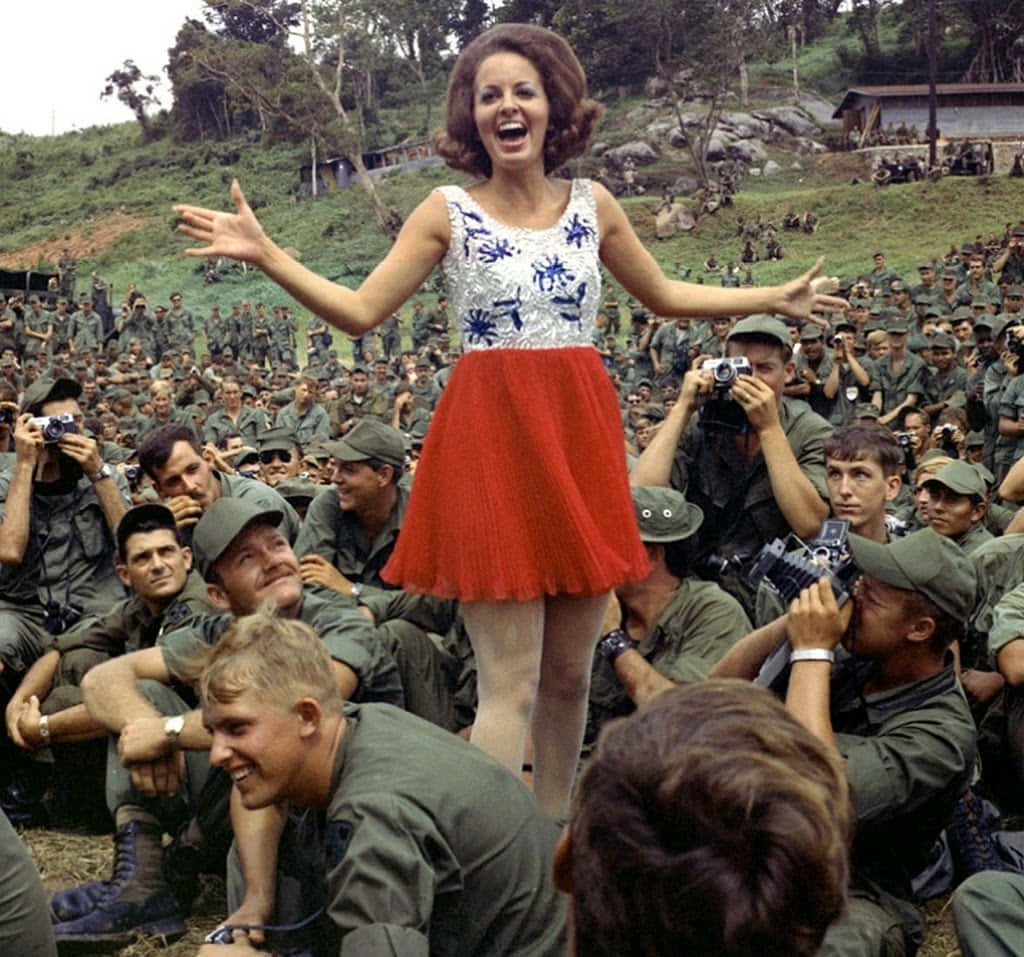 A Woman In A Red Dress Is Standing In Front Of A Group Of Soldiers