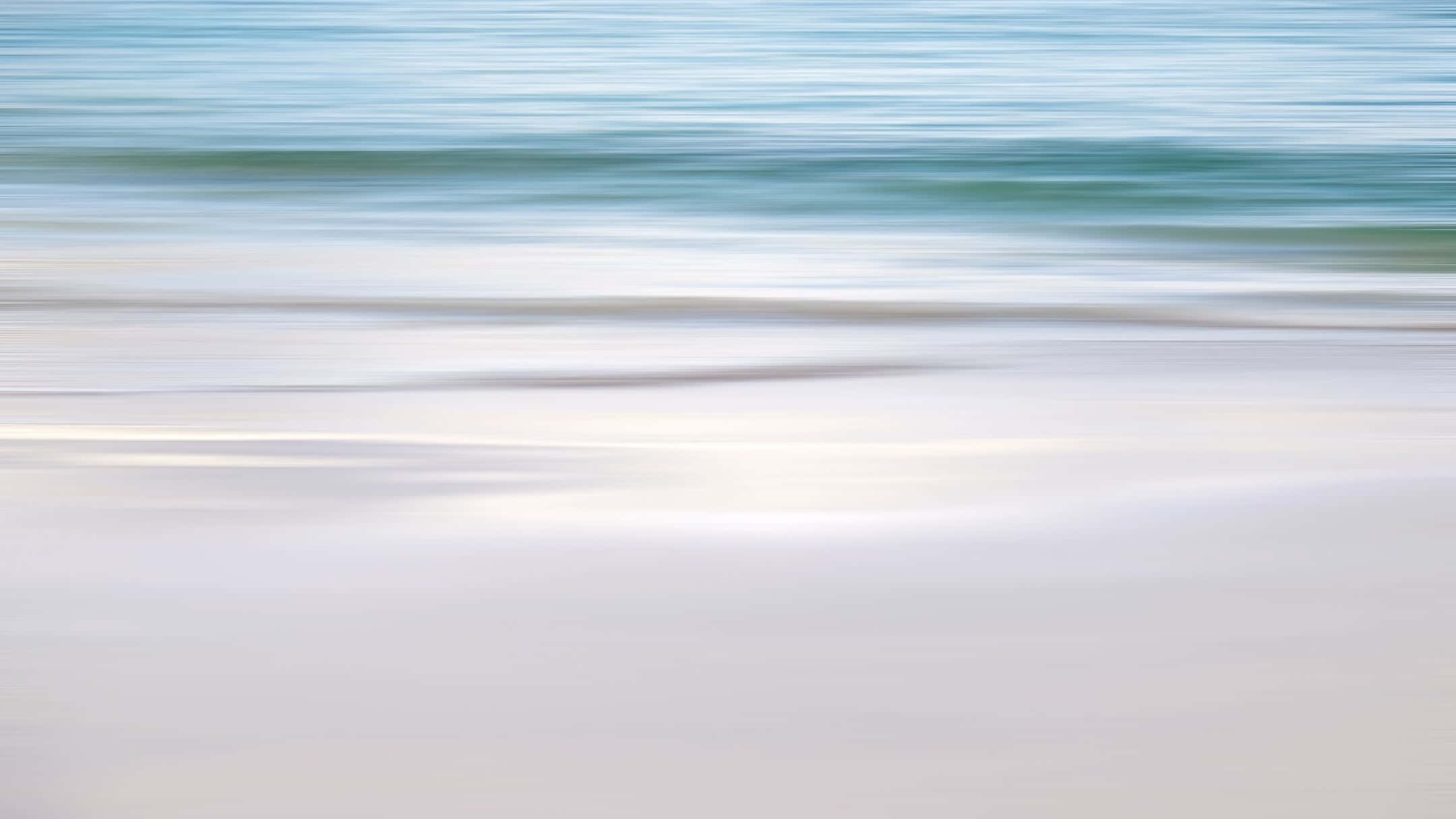 A Blurry Image Of A Beach With Water And Sand Wallpaper