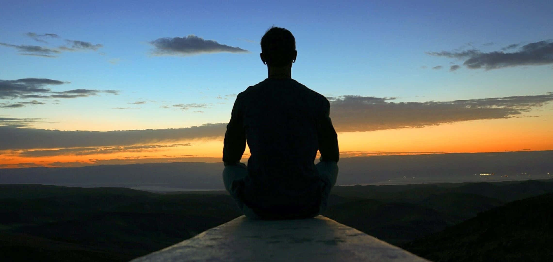 A Man Sitting On A Ledge Looking At The Sunset Wallpaper
