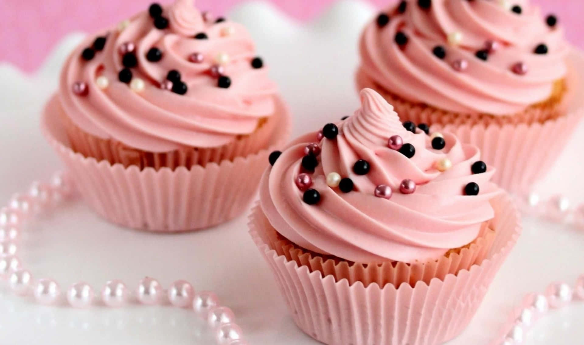 Three Pink Cupcakes With Black Sprinkles On Top