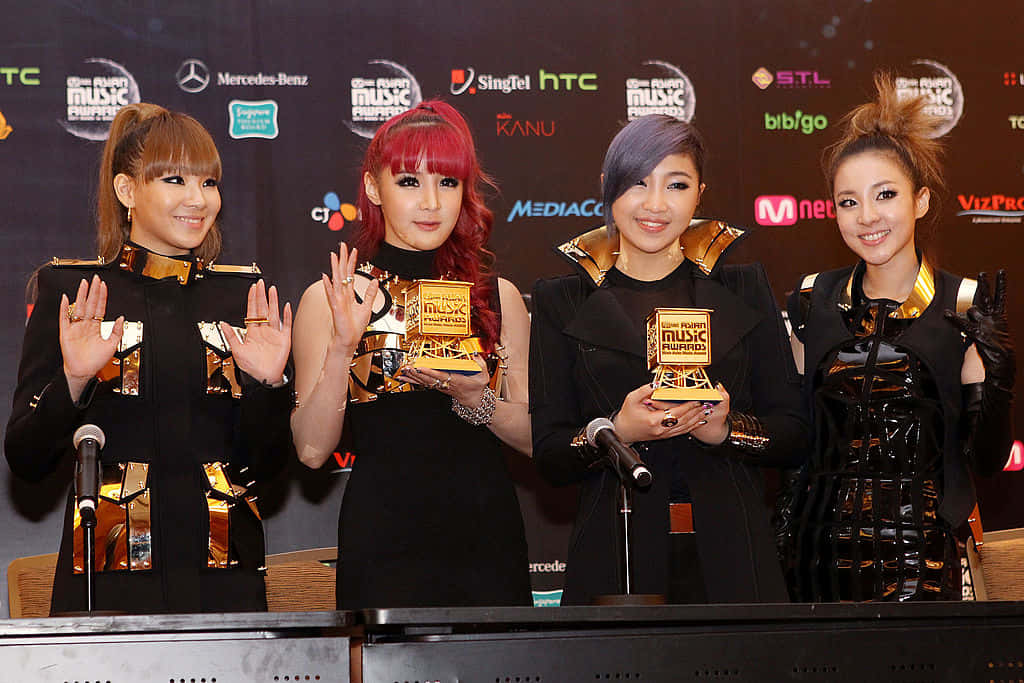 A Group Of Women Holding Awards In Front Of A Microphone