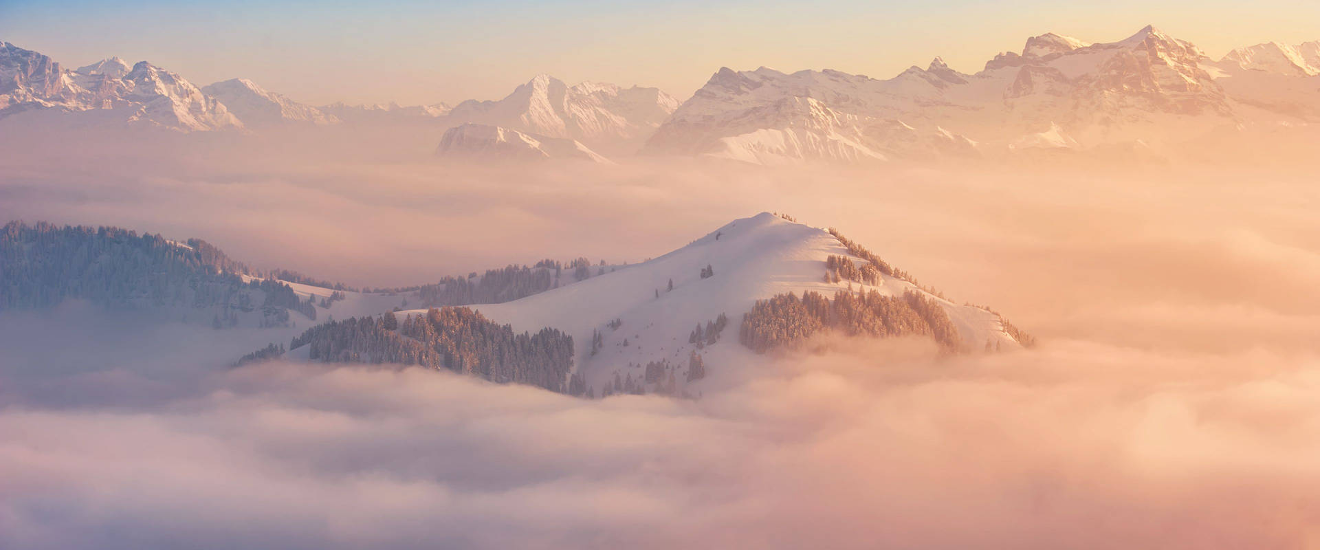 A Mountain Range Covered In Clouds At Sunrise Wallpaper